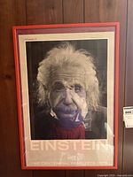 Frontal view of the framed Einstein poster against a wooden wall, showing the portrait and text.