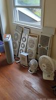 Photo of all fans and heater arranged on floor under window showing four vertical window fans, two oscillating fans, ceramic heater and ionizer.