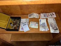 Shelf with various foreign currency bills and coins including piles of bills and a container with coins.