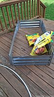 Full view of metal raised garden bed frame partially assembled on a wooden deck with three yellow bags of potting mix soil inside it.