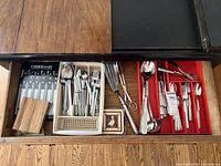 Drawer image showing Farberware steak knives in wooden block, trays with various forks, spoons, knives and serving utensils including ladle and tongs.