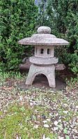 Full view of assembled pagoda on ground outdoors showing weathered surface and surrounding gravel and moss.