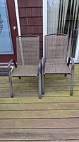 Front view of two metal legged patio chairs with plastic woven seats placed side by side on wooden outdoor deck.