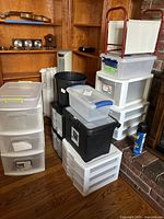 View of multiple plastic storage drawer units, lidded boxes, trash can, and magazine rack grouped on the floor by a fireplace.