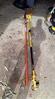 Two full-length pole saws laid out on concrete floor, one yellow Wagner electric with telescopic pole and one orange manual saw.