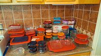 Wide view of Pyrex glass storage containers with various lids in orange, blue, and purple placed on countertop.