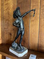 View of the full sculpture showing the boy with hat holding a crab and a shell on base, front