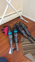 Photo showing four handheld vacuum cleaners on wooden floor next to a white object and brown rug.