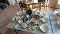 Photo depicting various dinnerware pieces including Villeroy and Boch cantered colorful patterned plates, bowls, mugs, and some plain white dishes.