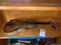 Full view of the violin showing its body, worn condition and missing strings.