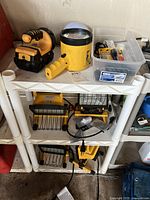Photo showing yellow handheld flashlight, headlamp, and other small lighting accessories on white plastic shelves.