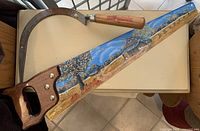 Image showing two antique agricultural tools: a hand saw decorated with colorful tole art on the blade and a curved scythe with a wooden handle.
