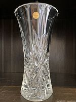 Front view of clear crystal vase with visible label on upper rim, showing flared top and intricate cuts.