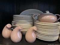 Stacks of speckled off-white dinnerware and pastel dusty rose droplet shakers on dark background