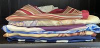 Side view of stacked silk scarves showing varied patterns and vibrant colors mostly including blues, purples, reds, creams, and browns.