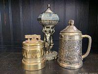 Photo showing three vintage brass decorative table top lighters with varied designs and patina.
