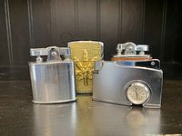Photo showing three vintage table top lighters with various finishes and a small clock integrated on one.
