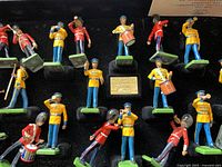 Close-up of metal military band figurines in red and yellow uniforms, posed with musical instruments and rifles on green bases.