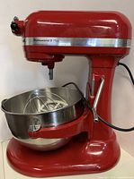 Front-left view of red KitchenAid mixer with stainless steel bowl and wire whip attached