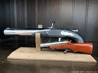 Side view of two vintage novelty lighters shaped like pistols on wooden base.