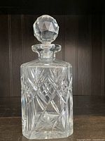 Full front view of the heavy cut crystal whiskey decanter with stopper on top against a dark wood background.