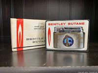 Vintage Bentley butane table top lighter displayed in original box on a dark surface with a dark background.
