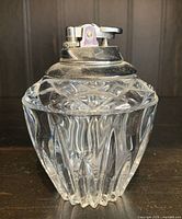 Front view of a vintage crystal glass table lighter showing clear faceted glass body and metal lighter top part.