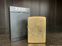Photo of a vintage Zippo brass lighter with detailed etched floral pattern on the front, and original black Zippo case.