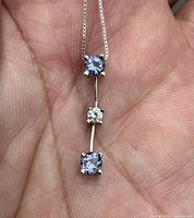 Handheld close-up of pendant showing two round tanzanites and center diamond