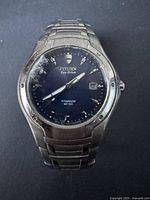 Front view of the Citizen men's watch showing the titanium case, bracelet, blue dial with Eco-Drive branding, and damaged cracked crystal on the left side.