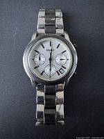 Full frontal image of a men's DKNY stainless steel watch on a dark background showing the dial, band, and bezel.