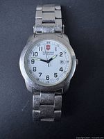 Front view of men's Victorinox Swiss Army watch showing white dial with black Arabic numerals and date window at 3 o'clock.