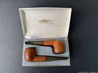 Two vintage tobacco pipes wrapped in brown textured leather, set in an original gray felt-lined box stamped with 'Longchamp France' in gold inside lid.