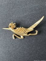Gold-tone vintage BOUCHER road runner bird brooch on dark fabric background showing textured details and black eye.