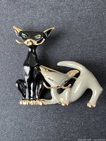 Close-up image of the vintage brooch showing black and grey cats with gold-tone details on a black textured background
