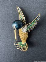 Front view of the hummingbird brooch showing gold-tone with green and black enamel and rhinestones on wings.