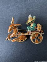 Full view of the brooch showing the donkey, cart, and figure with large hat and rhinestones on a black background.