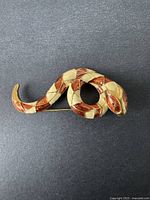 Front view of the vintage D'ORLAN snake brooch showing its coiled shape, cream and reddish-brown enamel segments, and red gemstone eye on gray background.