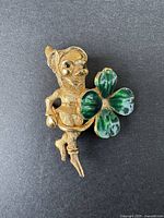 Vintage gold-tone leprechaun brooch with green enamel three-leaf clover on black background.