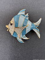 Front view of the blue and rhinestone fish brooch on a black background.