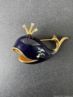 Front view of whale brooch showing dark blue enamel body with gold-tone metal edges and spout.