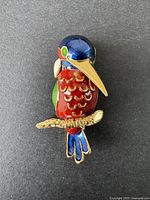 Front view of colorful enamel parrot brooch with blue, red, green, and gold tones.