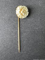 Full view of the vintage D'ORLAN flower brooch showing the carved flower atop the long stick pin attached to a dark background.
