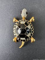 Front view of the turtle brooch showing the gold-tone limbs, head, black enamel shell, and clear rhinestones.