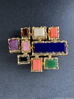 Vintage D'ORLAN brooch shown on a black background, displaying multi-colored rectangular and square blocks set in a textured gold-tone frame.