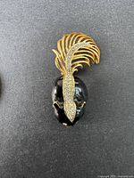 Front view of vintage D'ORLAN brooch showing black enamel face and gold-tone feather with rhinestones.