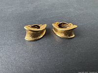 Two vintage D'ORLAN gold-tone clip-on earrings laid side by side on a dark background, showing the textured curved shape and front detail.