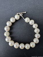 Bracelet laid flat showing round white pearls and clasp.