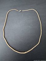 Full view of the pearl necklace laid out in a circular shape on a black background.