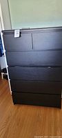 Full front view of the tall black dresser with six drawers showing the flat black melamine finish.